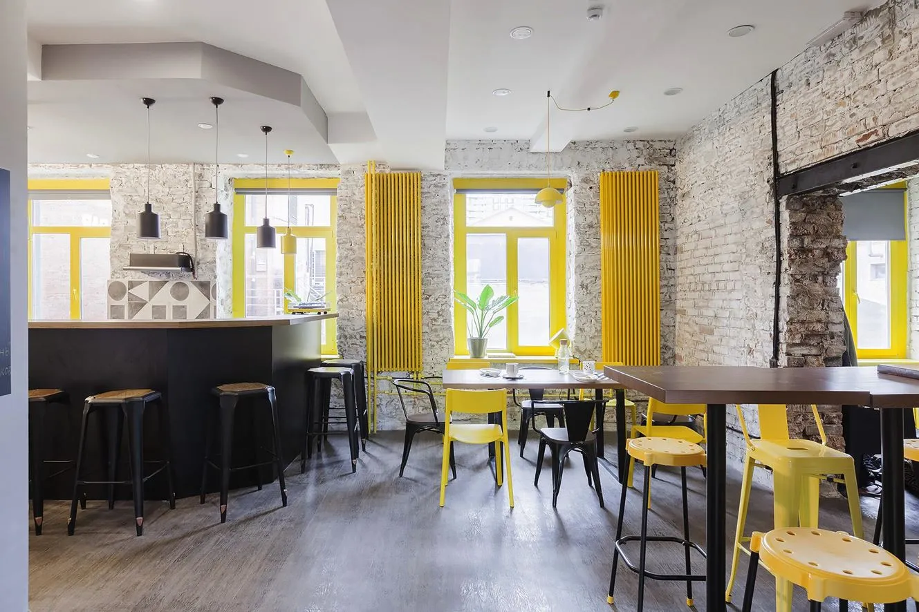 A cozy cafe interior with yellow accents, featuring wooden floors, brick walls, and bright yellow decor.