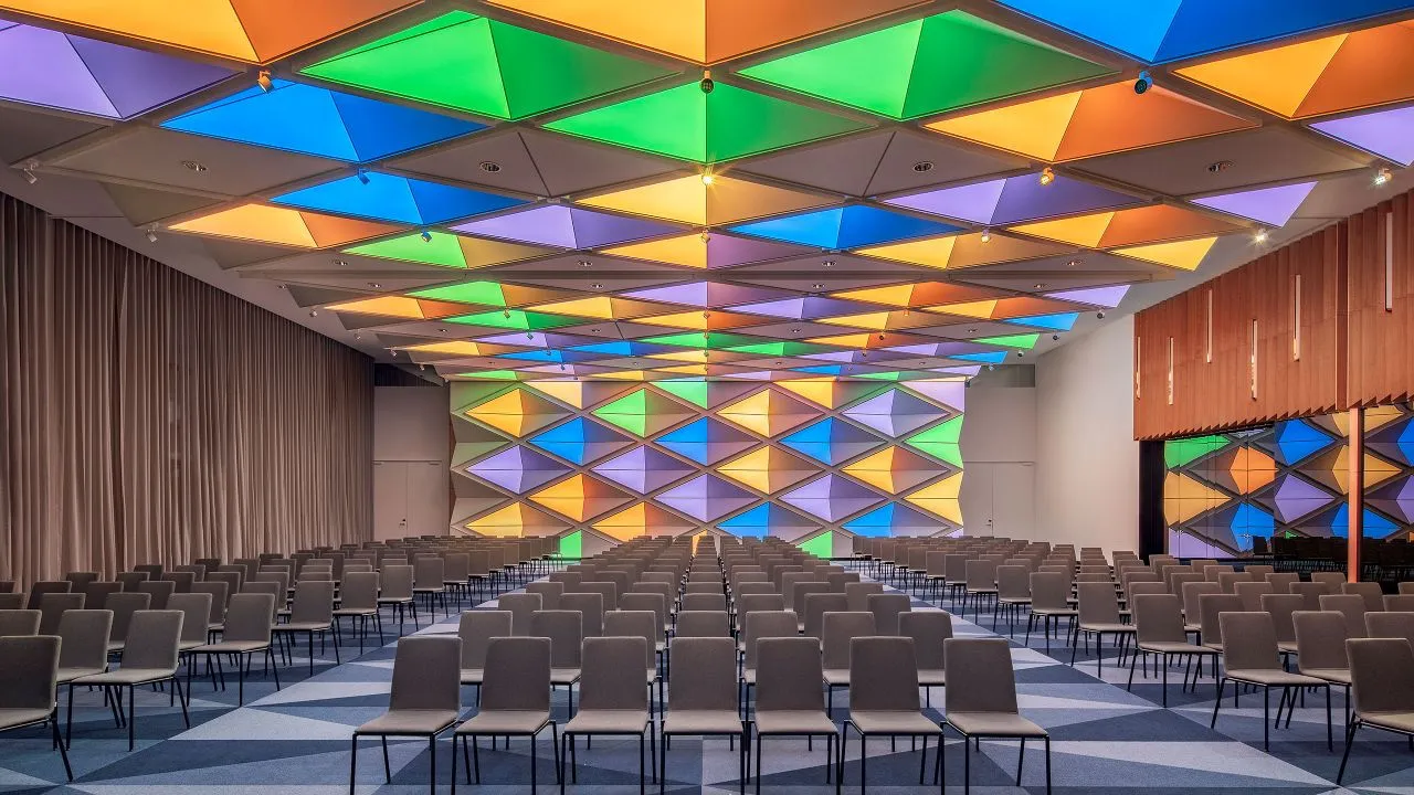 Conference room with chairs arranged in rows, multicolored ceiling panels, and a large colorful wall display.