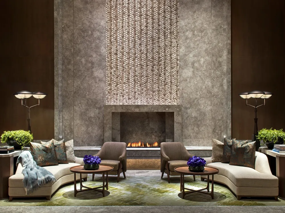 Modern hotel lobby featuring a fireplace, chairs, and tables with flowers.