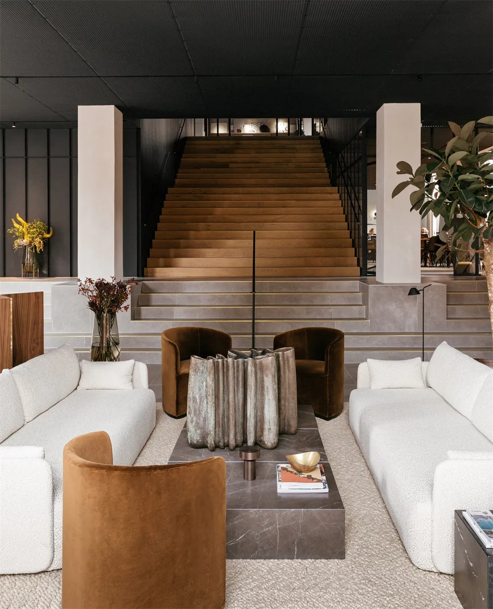 A modern lobby with a concrete structure, brown velvet chairs, and white couches.