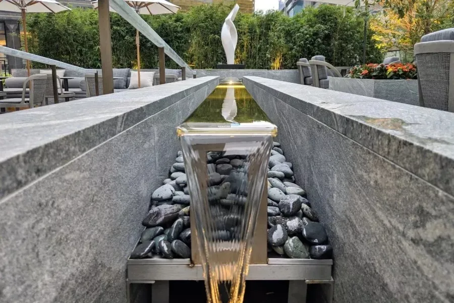 A minimalist water feature consisting of granite, stainless-steel, and glass materials, with a reflective glass element and s