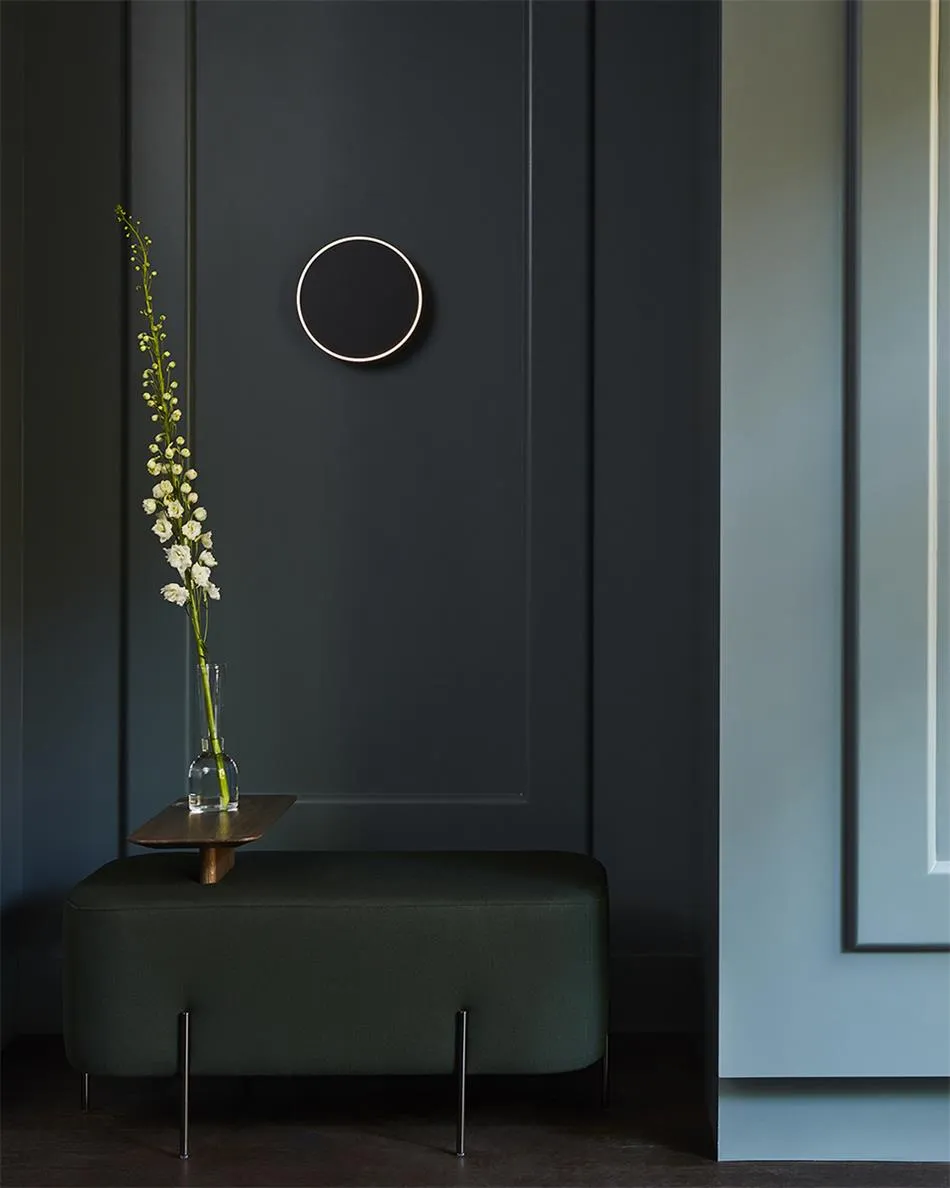 A modern entryway with a dark wooden bench and a vase of flowers placed on a small wooden table in front of a dark-paneled wa