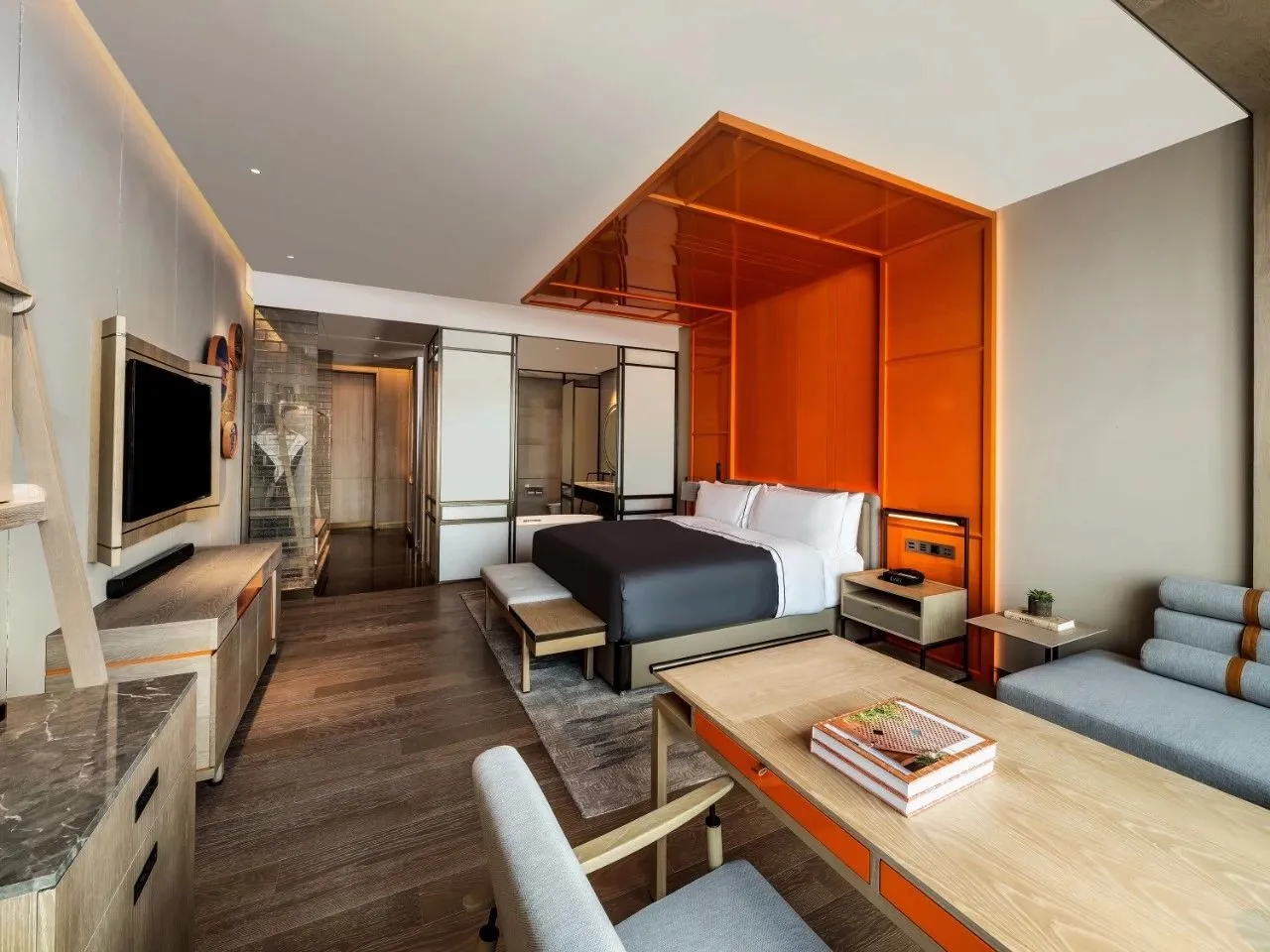 Spacious hotel room with modern design, featuring a wooden floor, metal accents, and glass partitions.