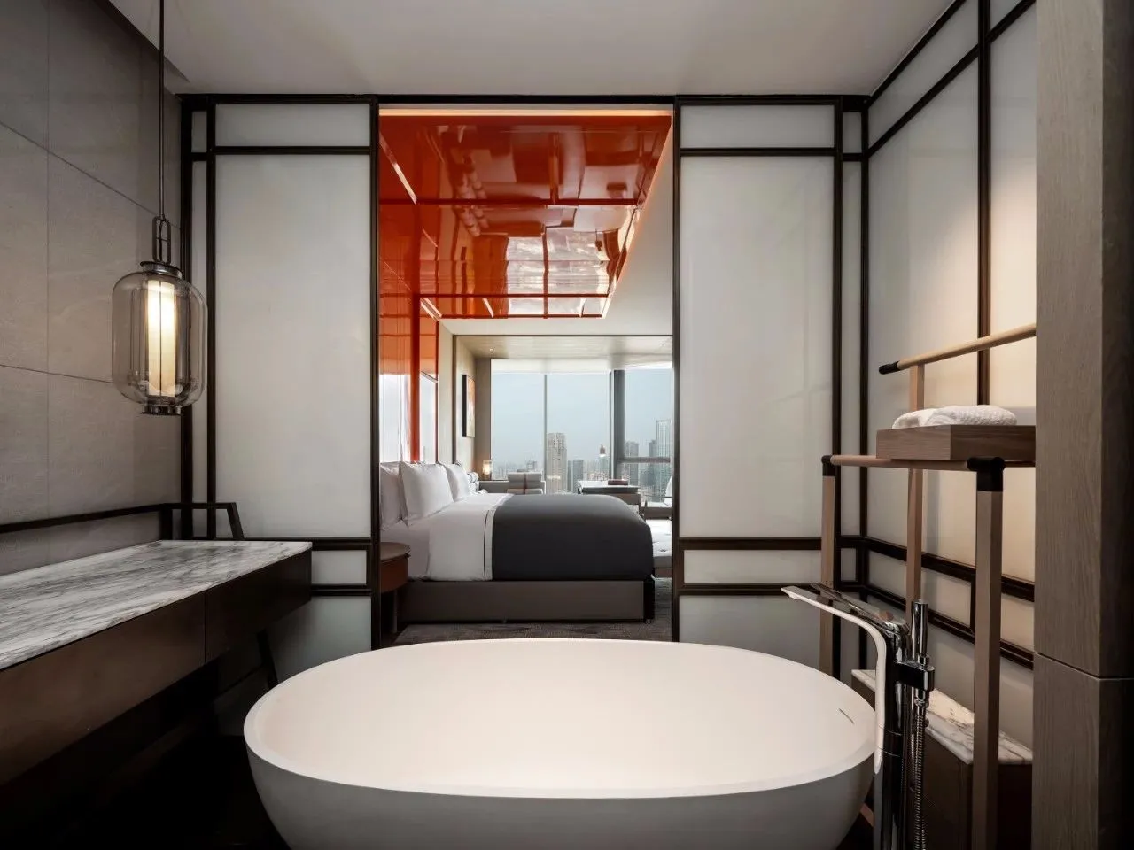 A modern minimalist bedroom featuring a circular bathtub, white walls, and a view of the city through large windows.