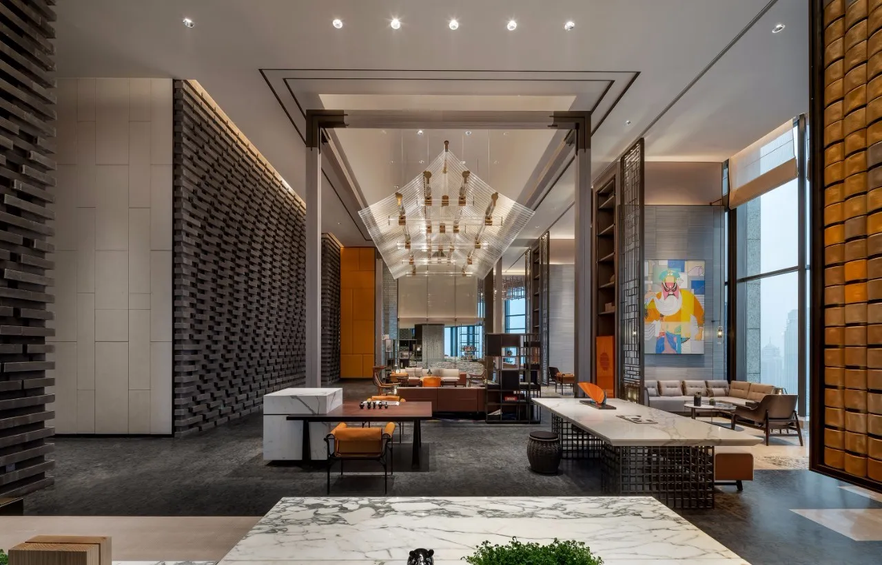 A spacious, modern lobby features a grand marble reception desk, metal chandelier, and contemporary seating.