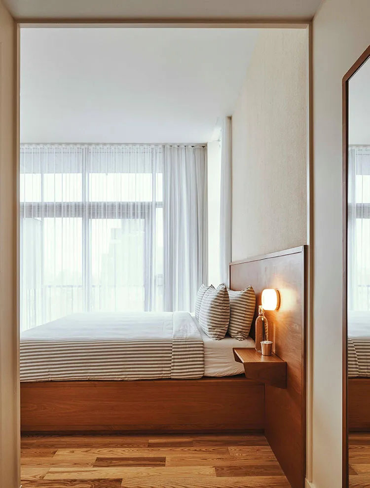 A modern minimalist bedroom featuring a wood-finished platform bed with striped bedding and a floating nightstand.