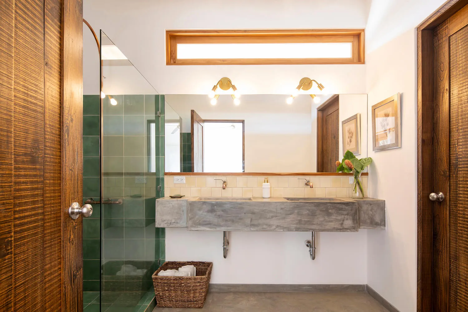 A modern minimalist bathroom with concrete walls and floors, a double sink vanity, and a walk-in shower enclosed by glass.
