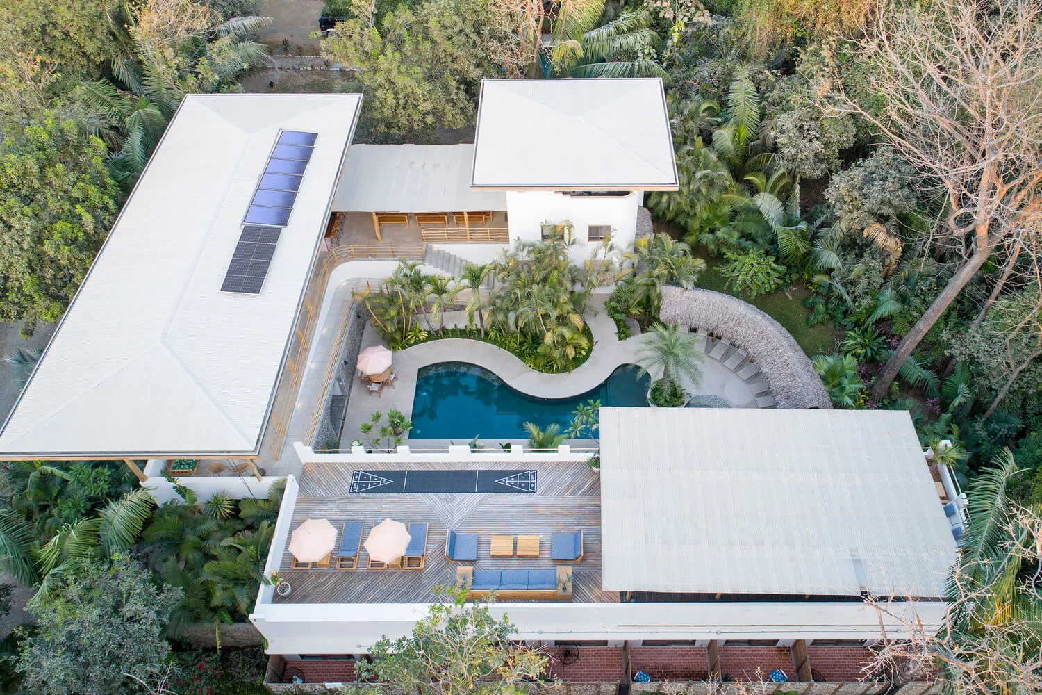 An aerial view of a modern residential house featuring a concrete pool surrounded by a lush tropical garden.