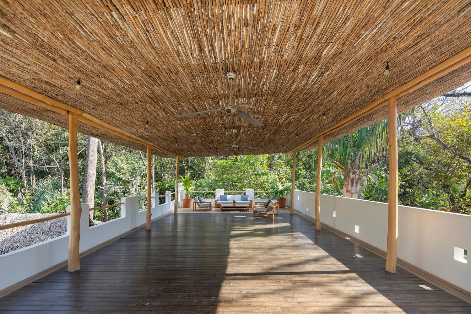 A modern living room with woven roof and wooden flooring surrounded by greenery.