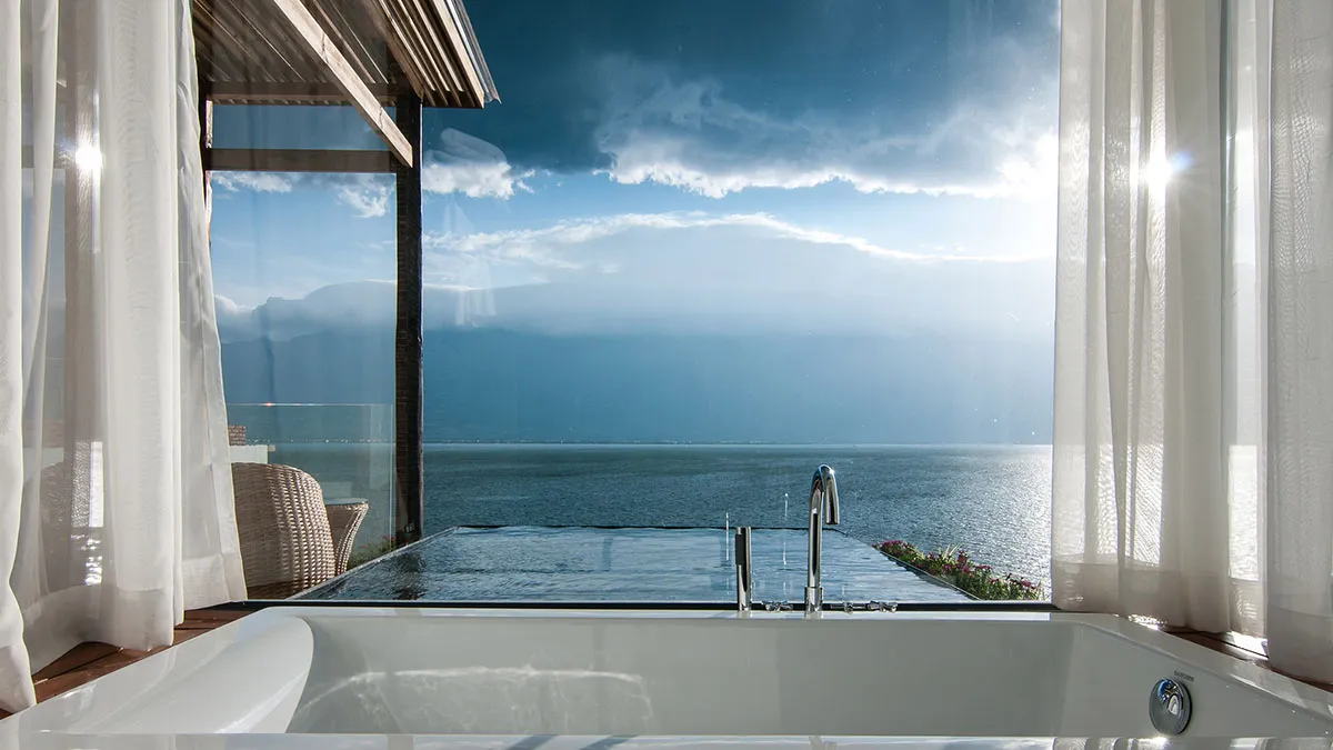 A luxurious hotel room featuring a modern bathroom with a white bathtub overlooking the ocean.