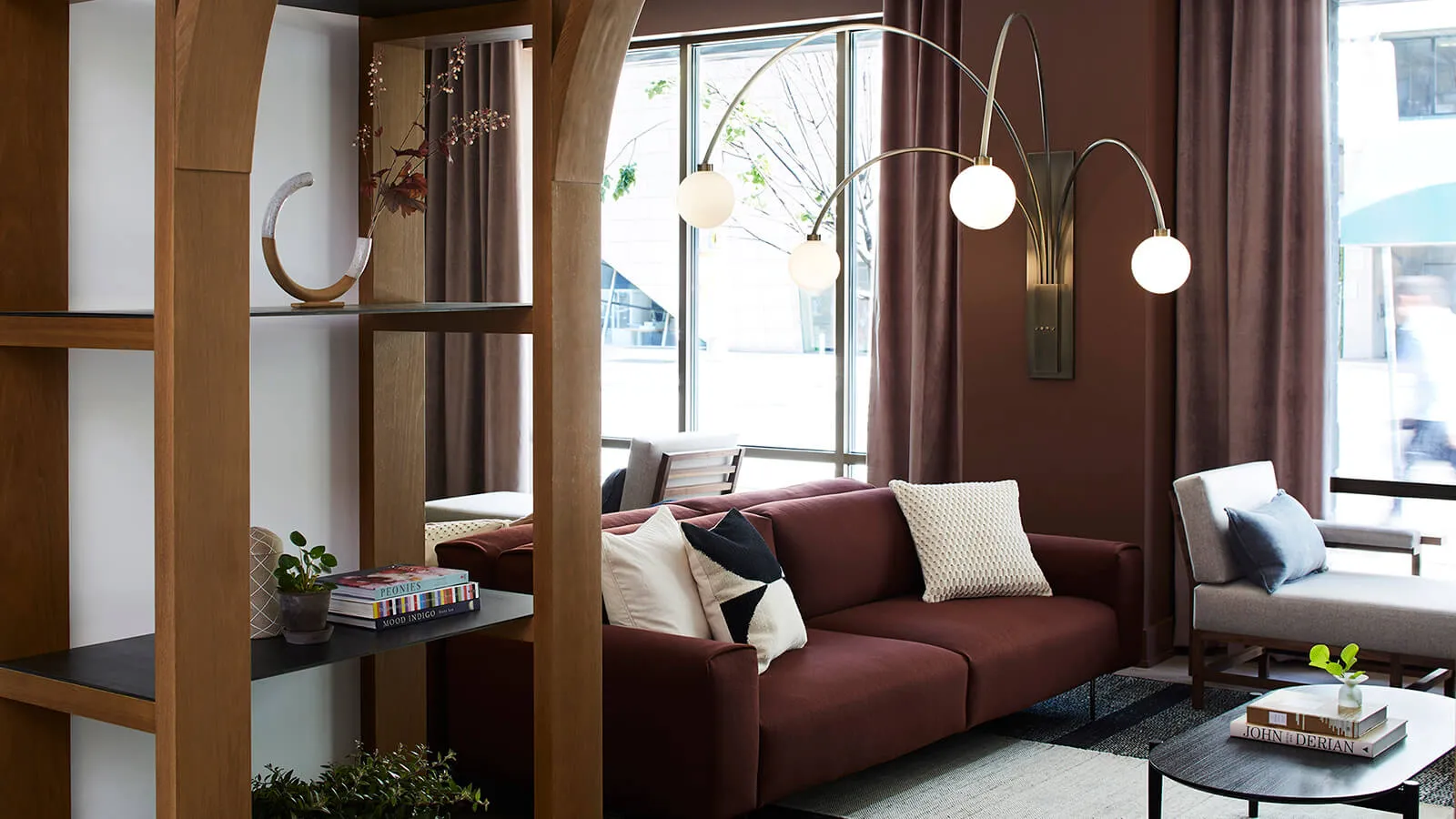 A cozy, industrial-style living room with a deep red sofa, white and black pillows, and a large floor lamp with multiple bulb