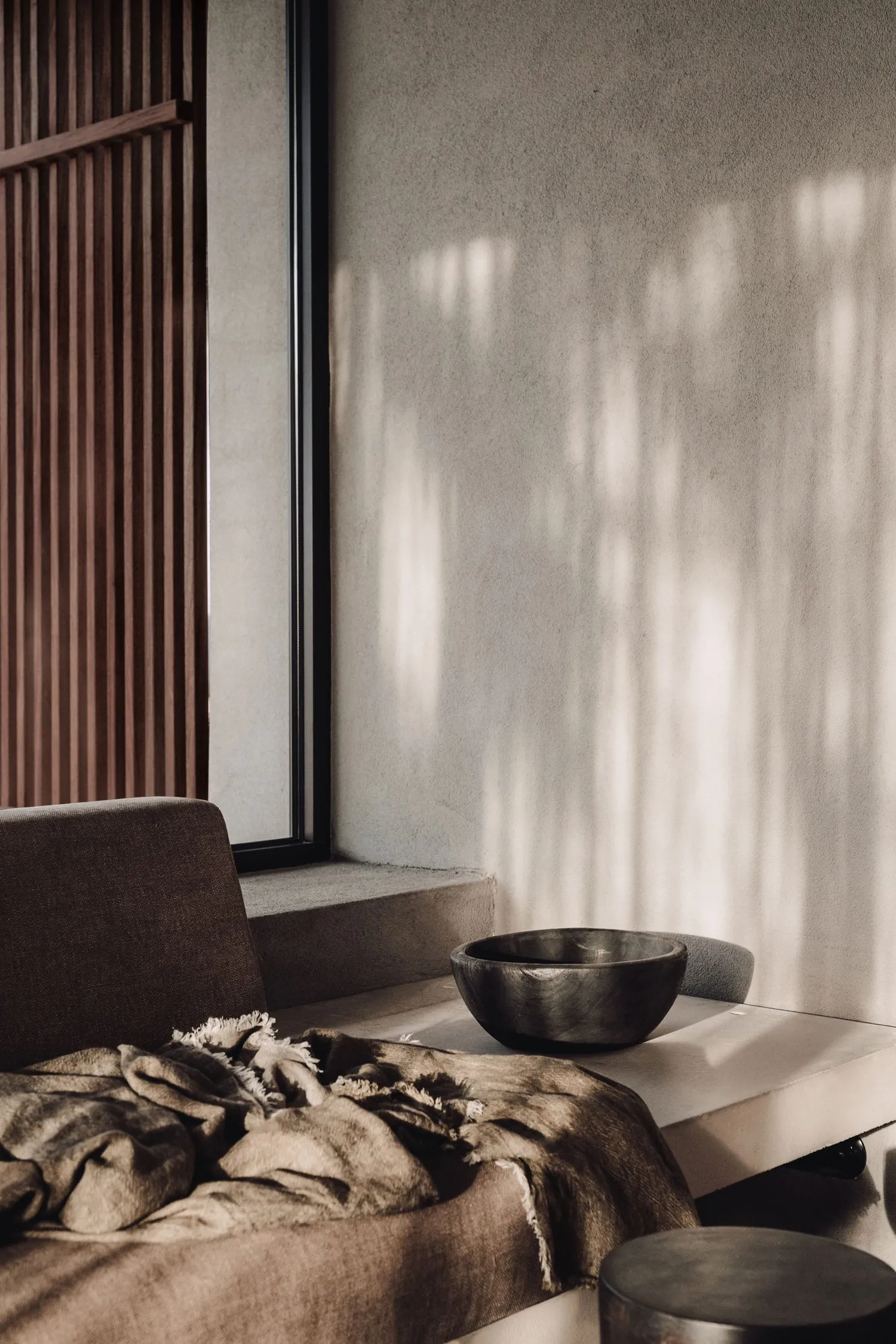 A minimalist living room featuring modern furniture on a concrete floor, with natural light streaming through a large window.
