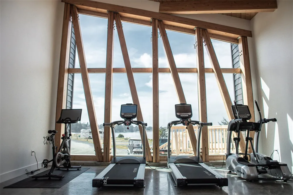 Industrial-style gym with metal treadmills and stationary bikes in front of large windows.