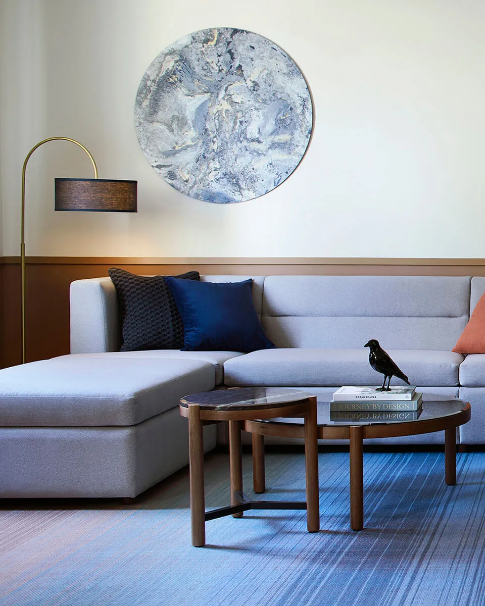 Modern living room featuring a sectional sofa with blue and gray upholstery, a glass coffee table, and a marble light fixture