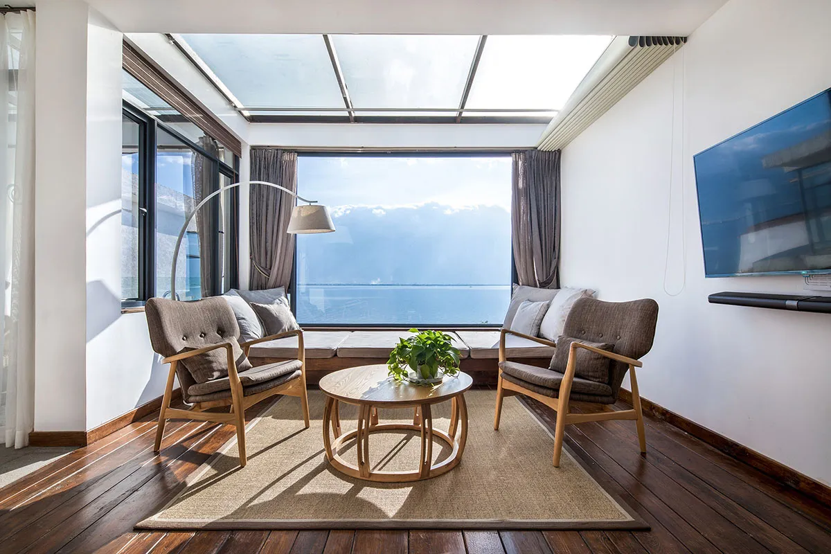 Modern living room featuring a comfortable sofa, table, and potted plant with a scenic marine view through large windows and 