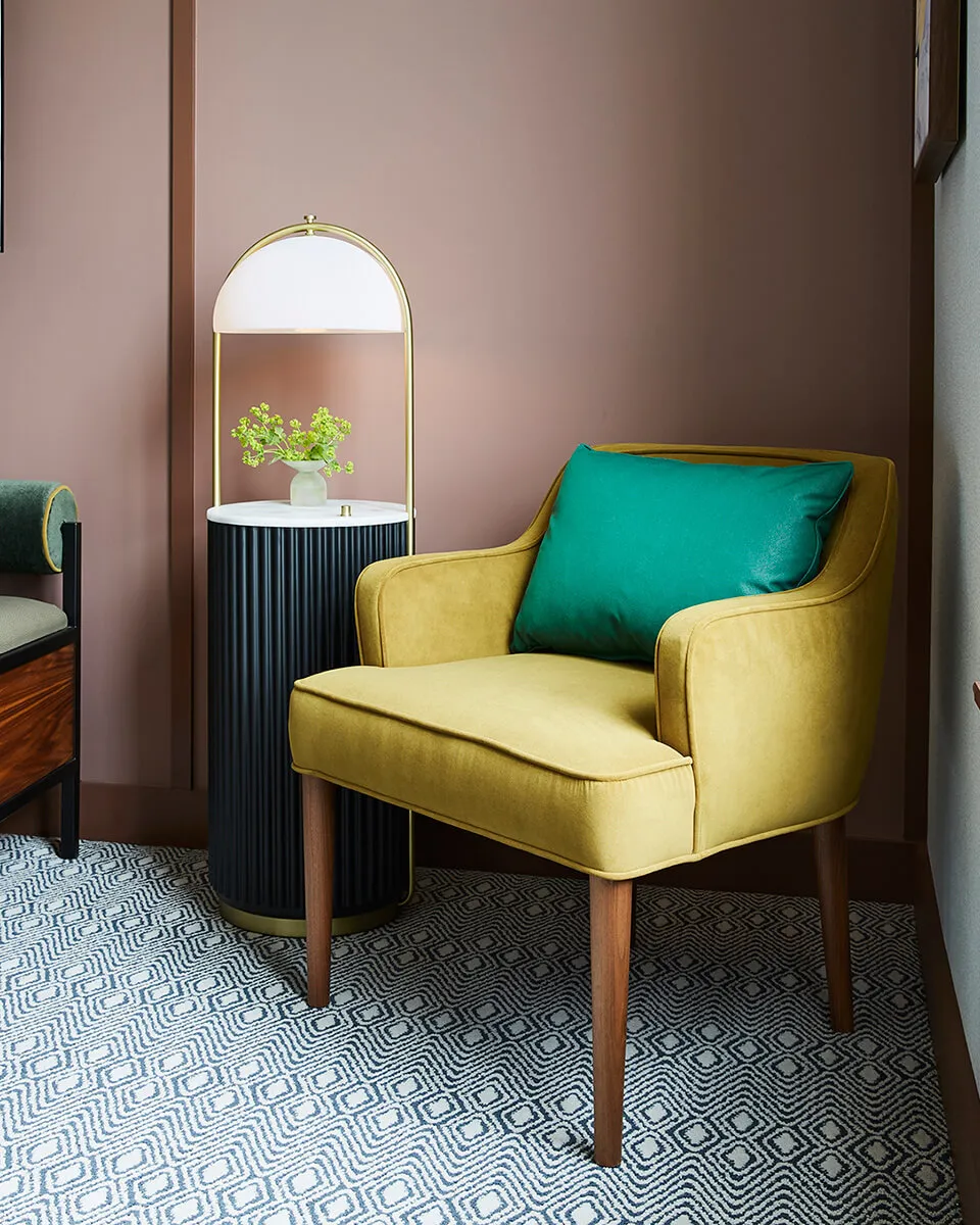 Modern living room with a yellow upholstered armchair featuring a green throw pillow, a marble side table with a brass lamp,