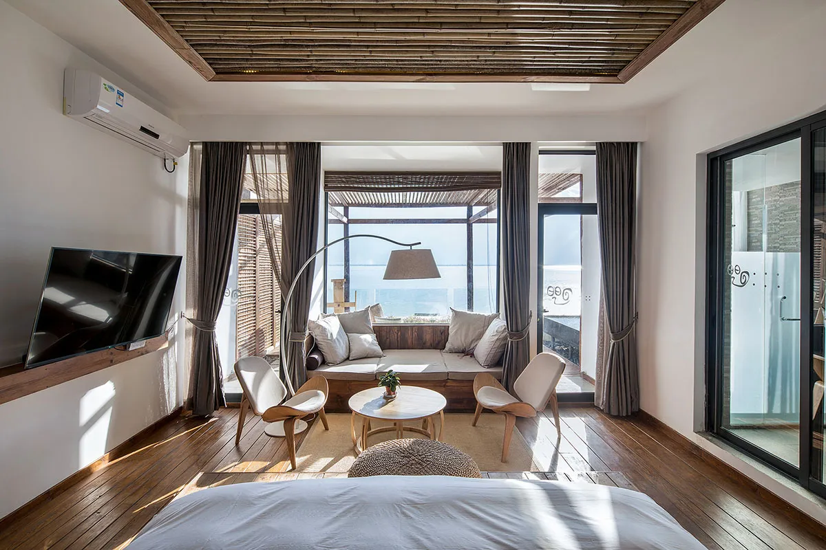 Modern residential bedroom featuring hardwood floors and upholstered furniture, with a view of the ocean and a seating area.
