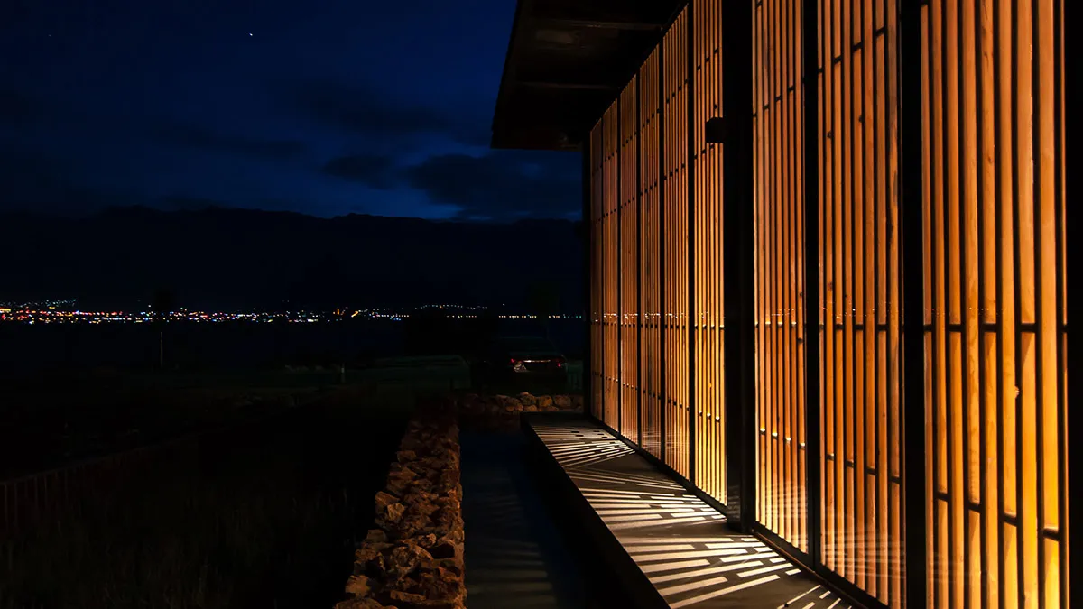 A modern residential exterior featuring wooden shutters and a stone pathway against a dark, starry sky.