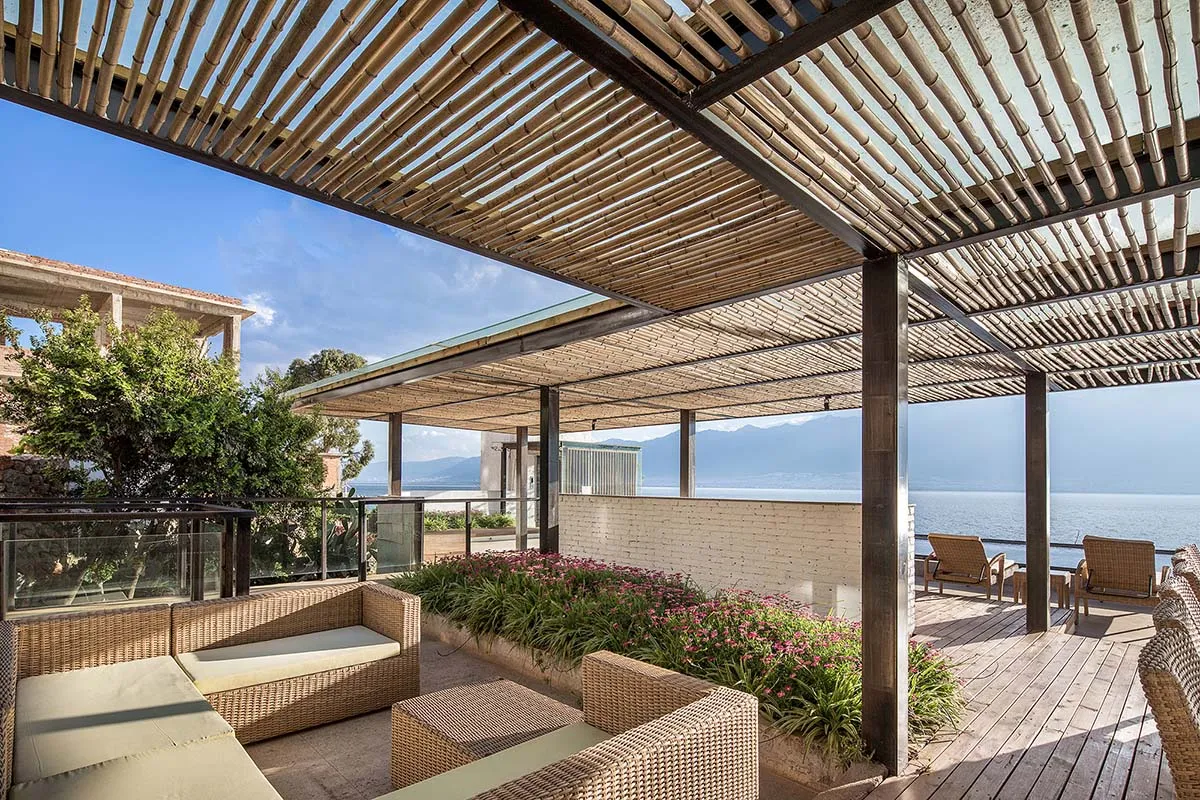 Modern rooftop landscape featuring wooden pergola and seating area by the sea.