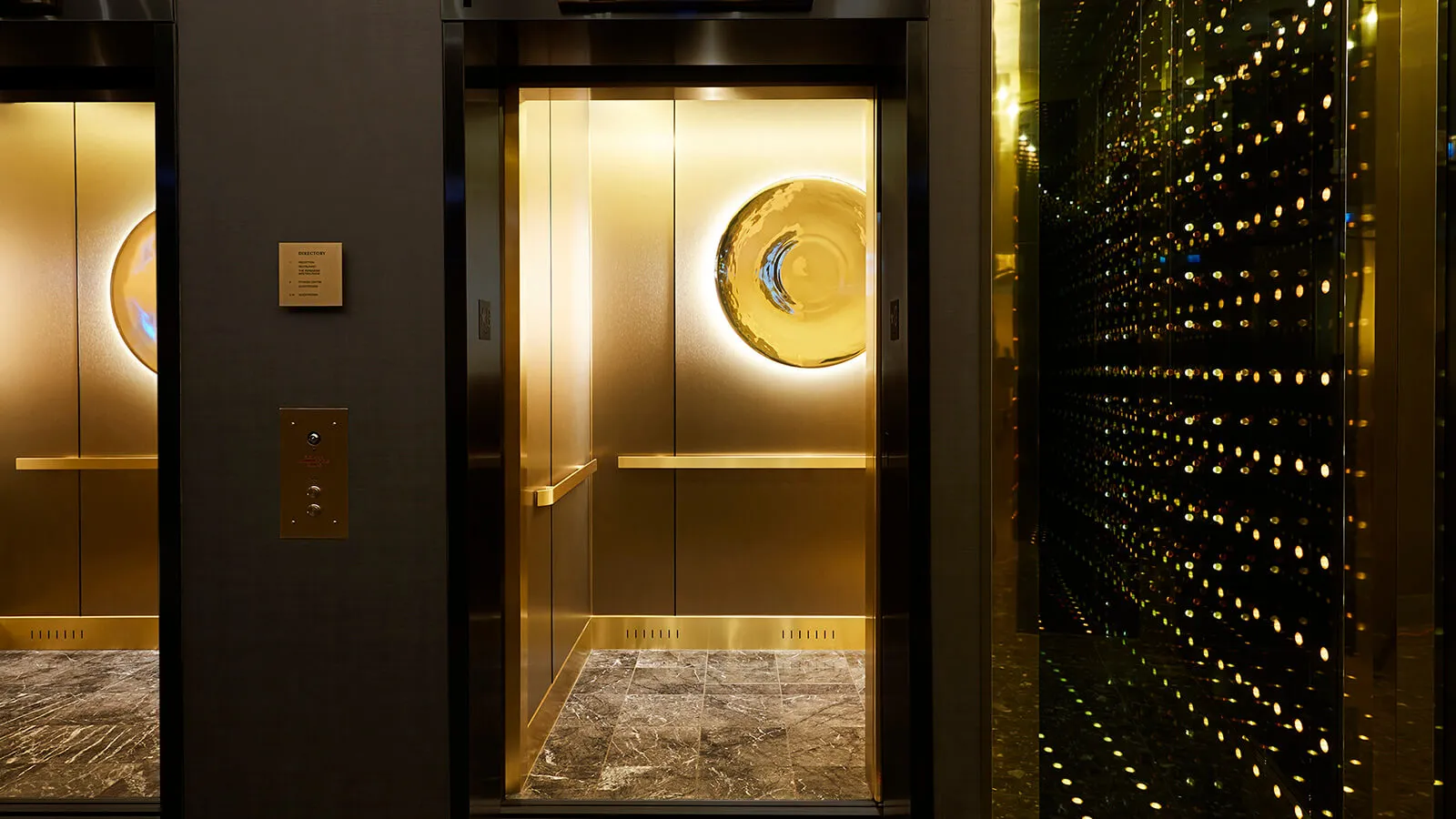 Modern elevator interior featuring a metallic sphere and marble floor.
