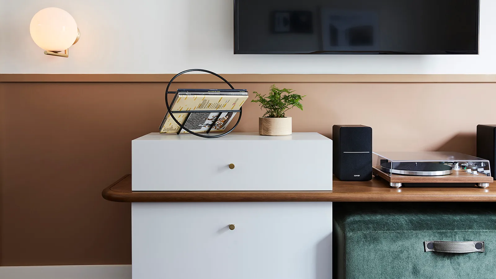 A modern living room featuring a white cabinet, wooden table, green ottoman, and a turntable with speakers.