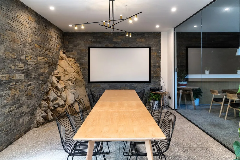 A modern industrial meeting room with concrete walls, wooden furniture, and a large white screen.