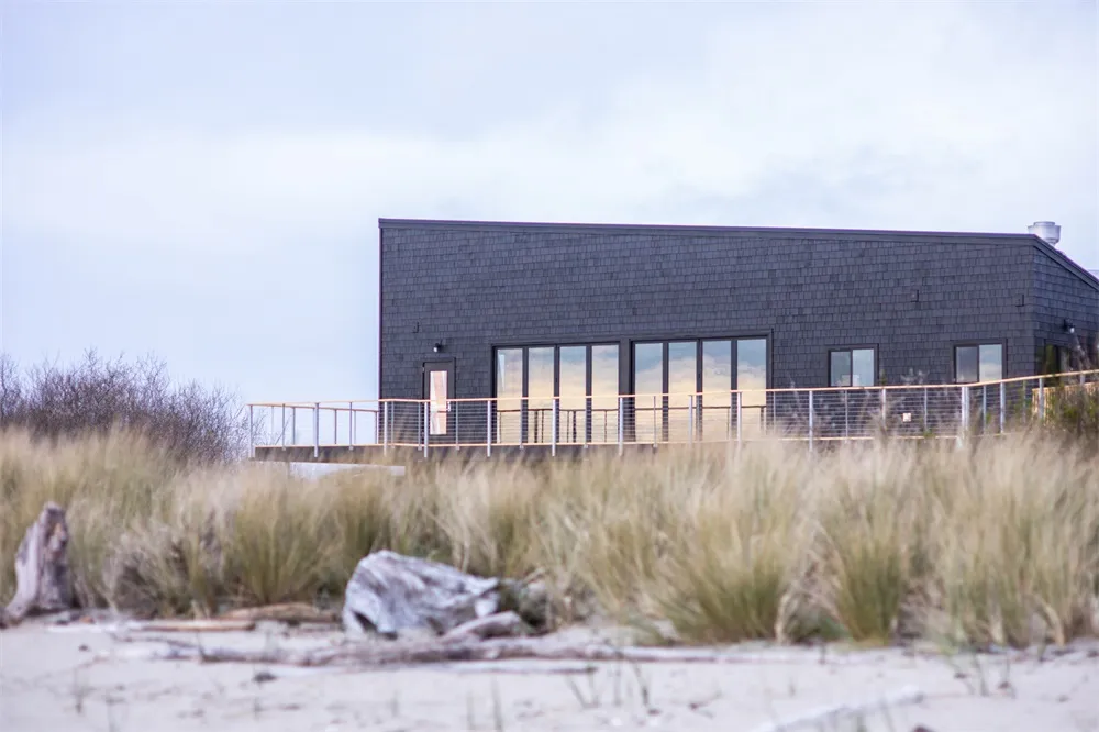 A minimalist beachfront house with black shingles and large glass windows.