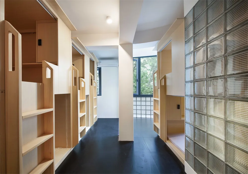 A hallway in an industrial-style apartment featuring wooden shelves and glass block walls.