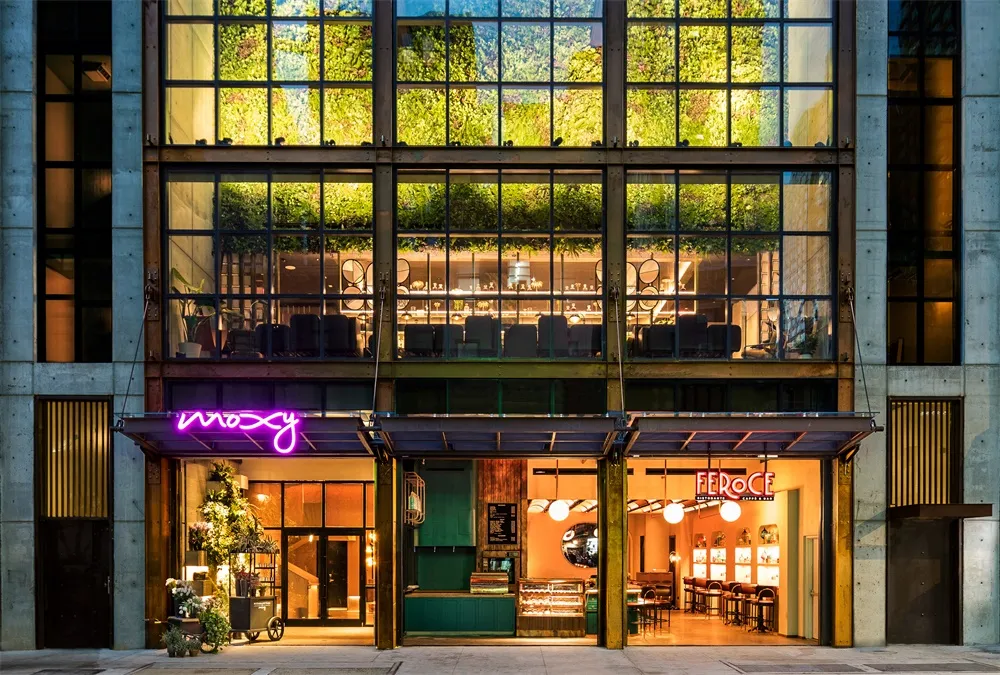 A modern cafe interior featuring concrete, glass, and greenery.