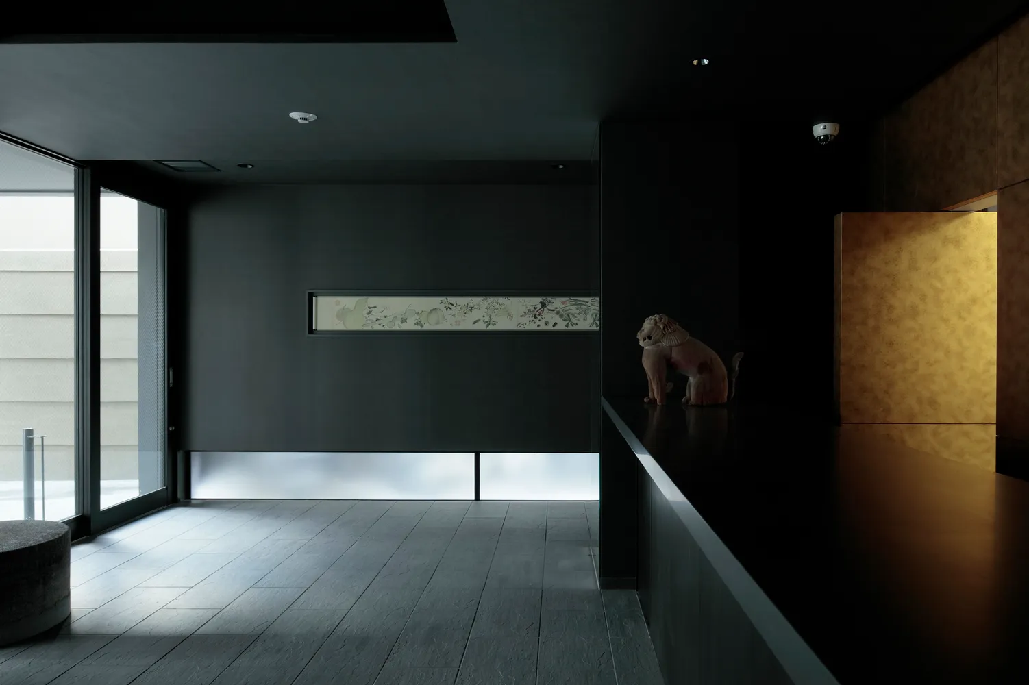 A minimalist interior with concrete walls, a black floor, and a small sculpture.