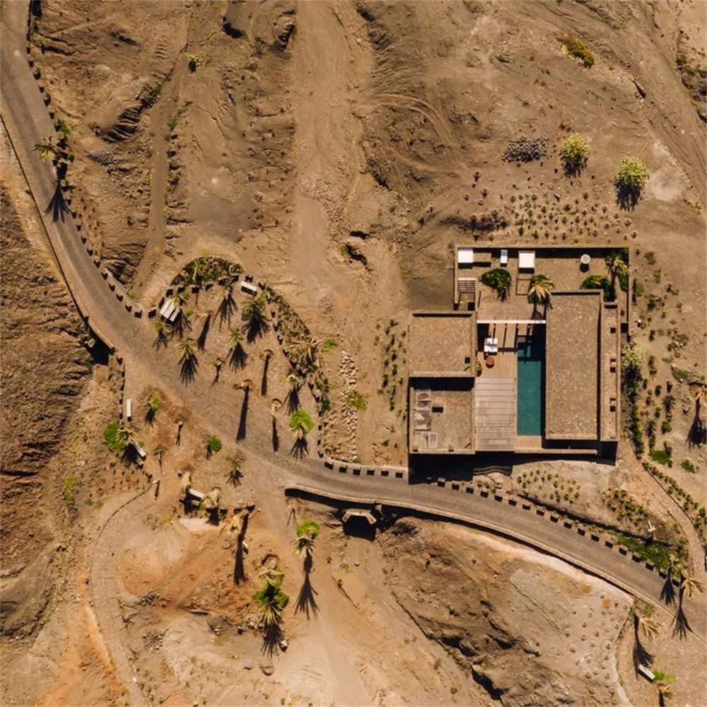 Aerial view of a modern, minimalist concrete house with a pool, located on a desert landscape.