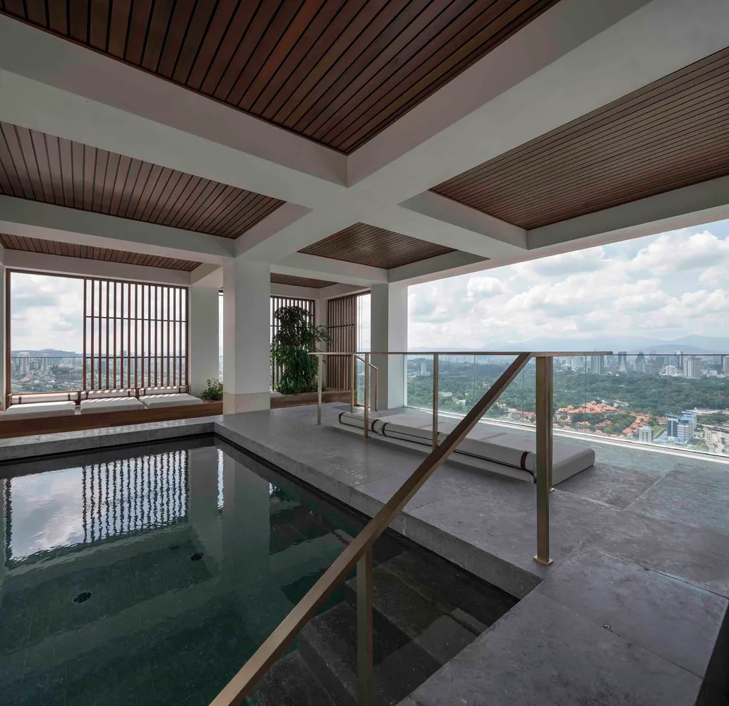 A modern indoor pool deck features concrete flooring and glass railings with a view of the cityscape.
