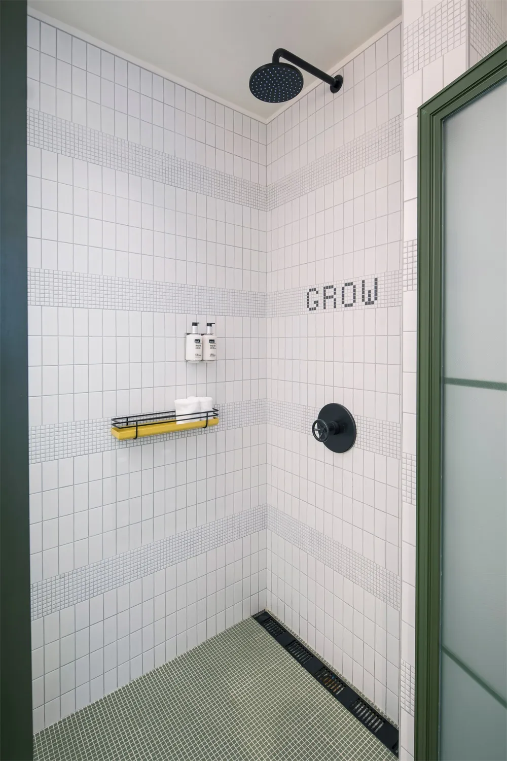 Industrial-style bathroom with white tiled walls, yellow shelf, and black shower faucet.