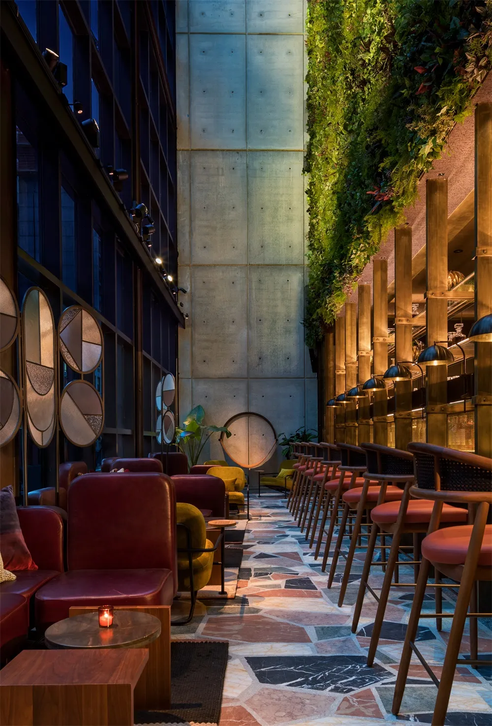 A modern bar with concrete walls, glass partitions, and wooden stools and tables.