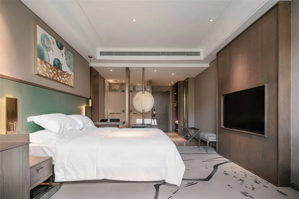 A modern minimalist bedroom with a clean white bed, green headboard, and artwork on the wall.