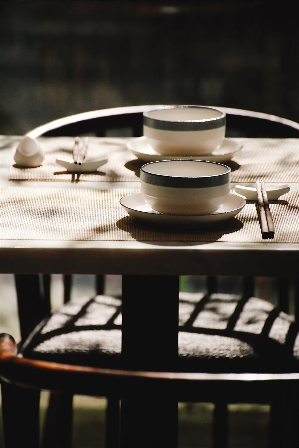 A set of ceramic dinnerware on a table with place mats and chopsticks.