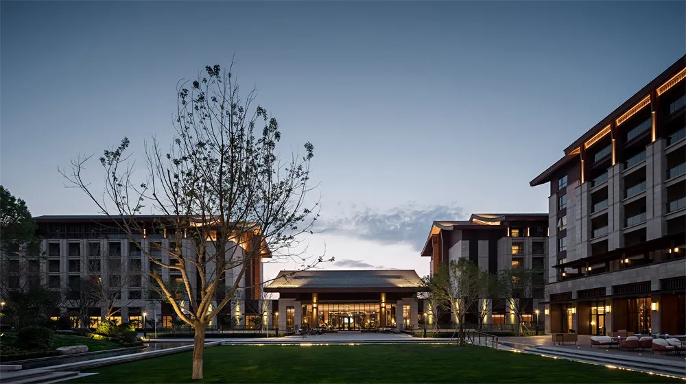 An illuminated entrance to a modern hotel exterior during dusk, featuring contemporary architectural design with warm lightin