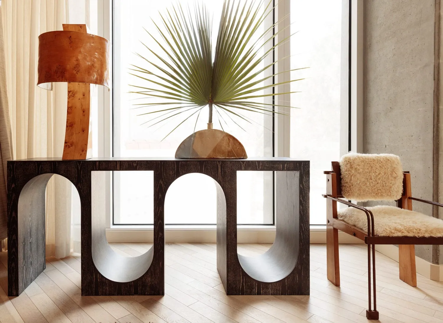 A modern interior space featuring a wooden and glass console table, a potted palm plant, and a fur-covered chair.