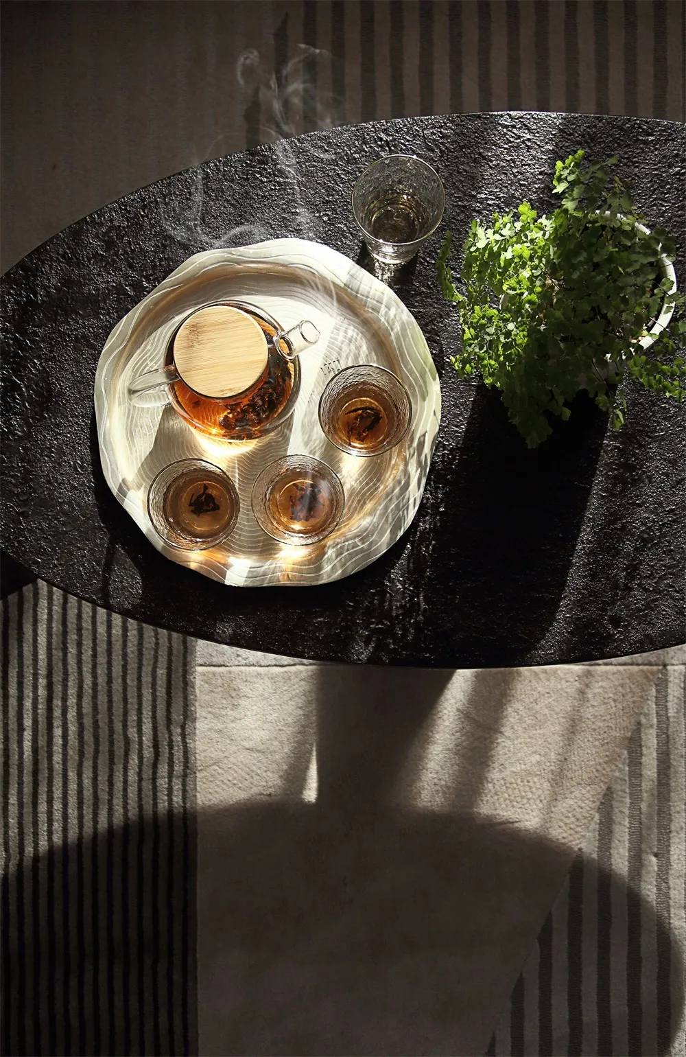 A modern coffee table setting with a glass teapot and cups, placed on a black stone surface.