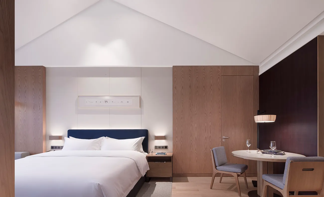 Contemporary minimalist bedroom featuring a bed with a navy headboard, white bedding, and a wooden wardrobe.
