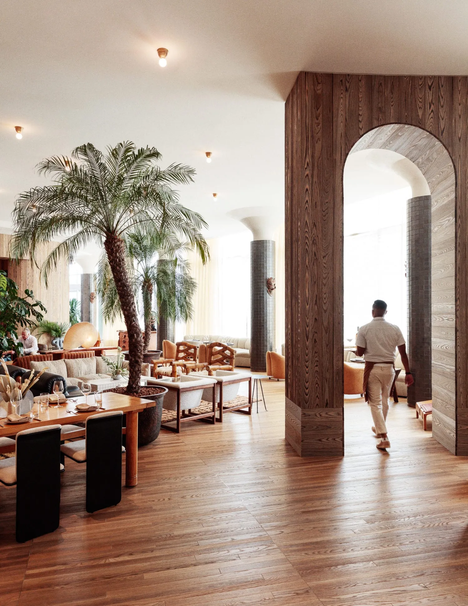 Modern restaurant interior with wooden walls and furniture, plants, and contemporary decor.