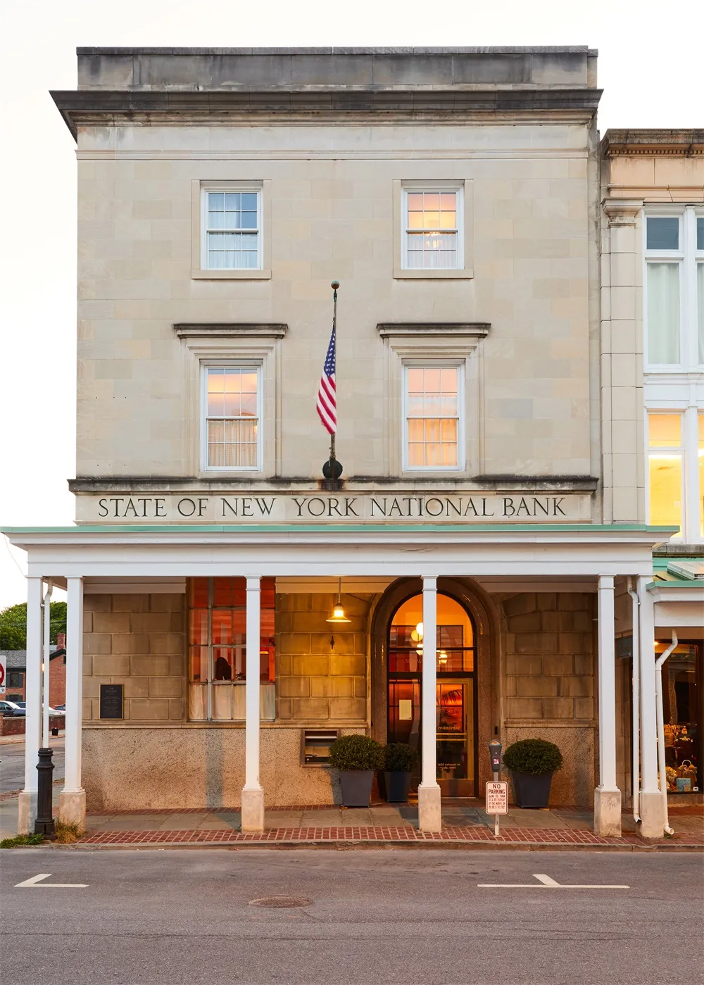 The exterior of the New York National Bank, featuring stone cladding and an American flag.
