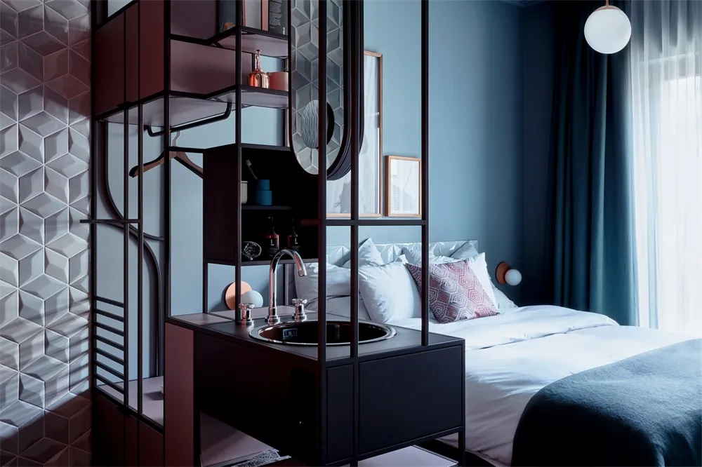 A modern bedroom features a metal and glass vanity unit with a sink and mirror, complemented by a comfortable bed with white 