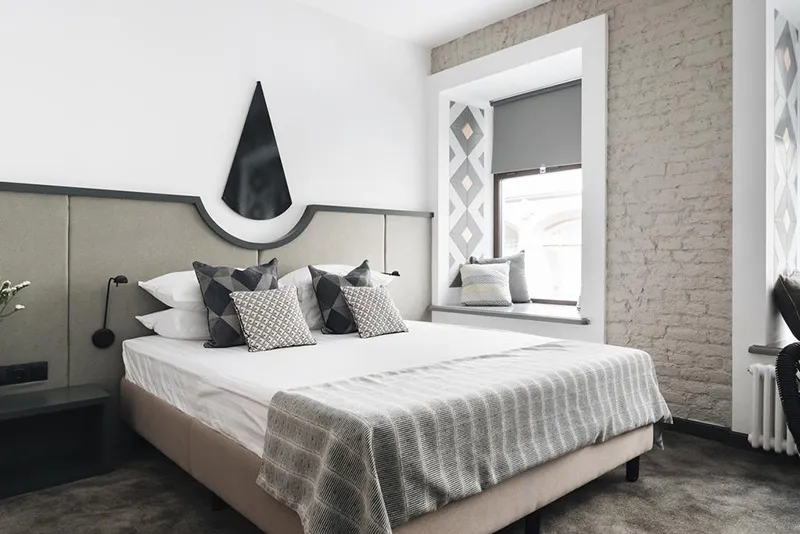 Modern minimalist bedroom with concrete walls, fabric bedding, and wooden accents.