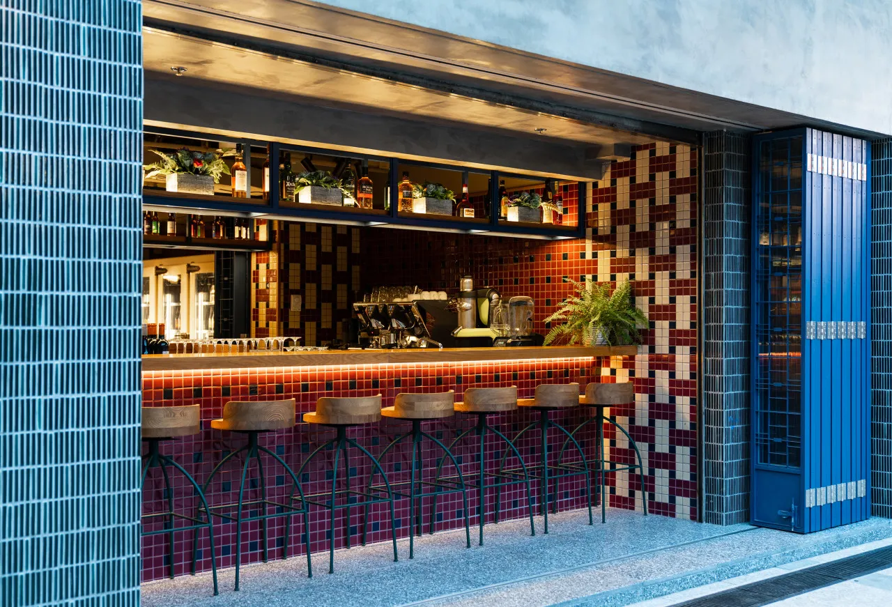 A modern bar counter with a multicolored tiled backsplash and wooden stools.