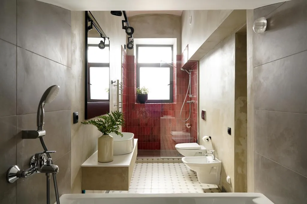 A modern bathroom featuring red and white ceramic tiles with a white freestanding bathtub, a white toilet, a white bidet, and