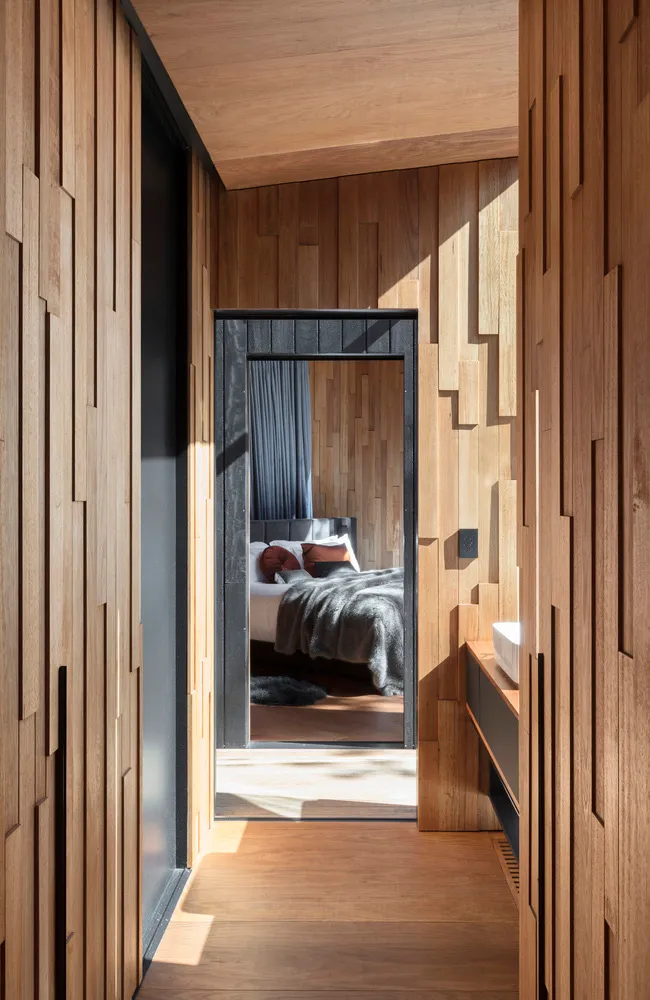 Modern bedroom with wooden interior design, featuring a bed with white sheets and orange pillows, framed by wooden walls and