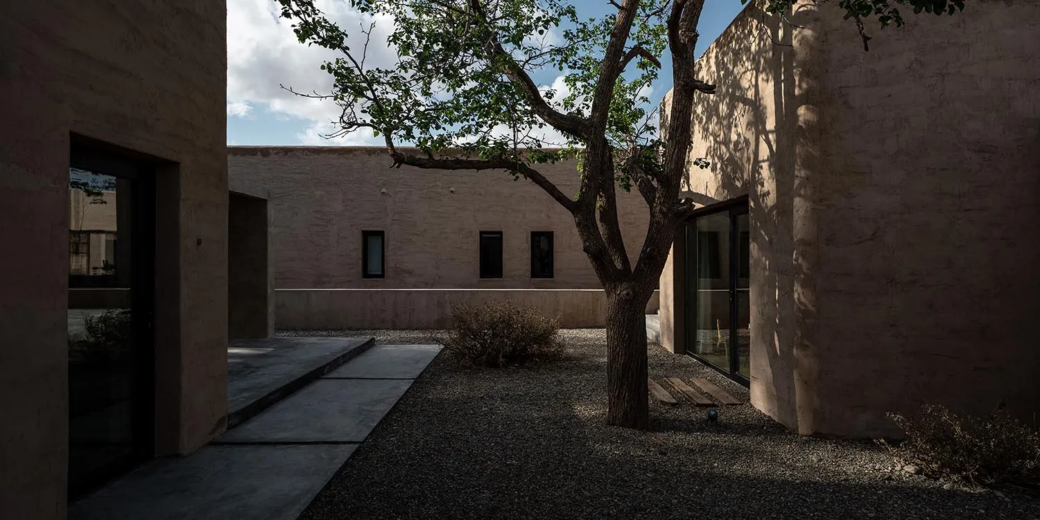 Modern garden featuring concrete walls, gravel pathway, and glass doors with a tree and vegetation