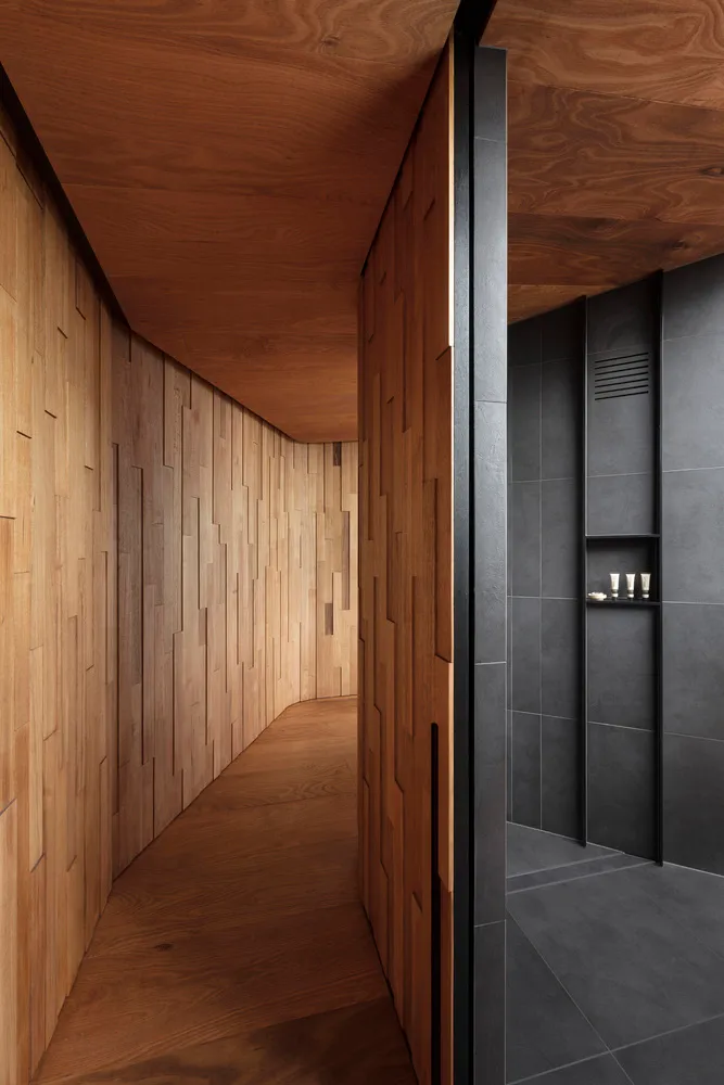 A modern minimalist bathroom with wooden paneling and dark gray tiles on the walls and floor.