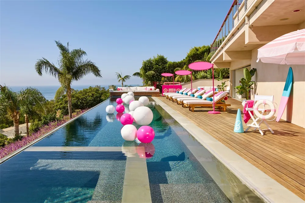A minimalistic swimming pool deck with lounge chairs, umbrellas, and large balloons in the pool.